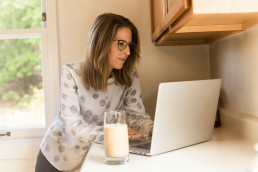 Une femme debout dans sa cuisine travaille sur son ordinateur - elle rédige un bon dossier RAEP